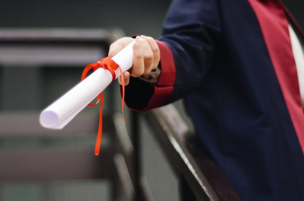 person-holding-white-scroll-2292837 A close-up image of a graduate holding a diploma tied with a red ribbon, symbolizing achievement and success.